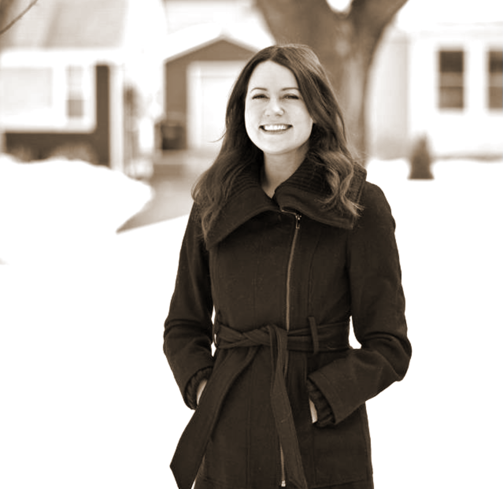 photo of a woman smiling and standing outside with hands in her pockets, with a snowy neighborhood in the background